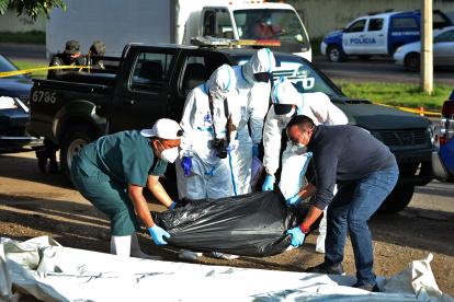 Officials of the Police Board of Investigations (DPI) help employees of the Forensic Medicine Board pick up a black plastic bag containing a corpse in a street in Tegucigalpa on August 19, 2020. - Corpses appeared again in the streets in an upturn of violence in northern Central America, after a truce in the beginning of the new coronavirus pandemic, when social isolation measures were taken to prevent contagions. (Photo by ORLANDO SIERRA / AFP)