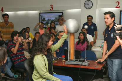 En una clase de Física, una alumna toca una esfera eléctrica. Los grupos de trabajo deben estimar el voltaje que recibió y explicarlo. Al fondo, el profesor Florencio Pinela.