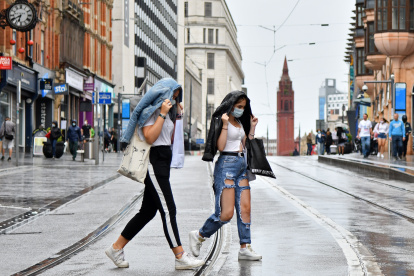 Two women wearing protective face masks cross tram tracks in the rain in Birmingham, central England on August 22, 2020, as Britain"s second-city, home to more than one million people, was made an "area of enhanced support", because of concern about a spike in cases of the novel coronavirus. (Photo by JUSTIN TALLIS / AFP)