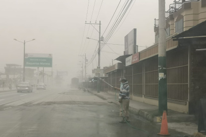 Ciudadanos en el cantón Jujan, del Guayas, esparcen agua en la calzada para evitar la dispersión de la ceniza.
