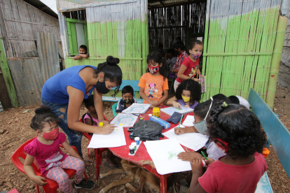 En una casa de caña, con pisos de tierra, 20 niños reciben ayuda educativa en la cooperativa Realidad de Dios. Líderes comunitarios colaboran en la tarea.