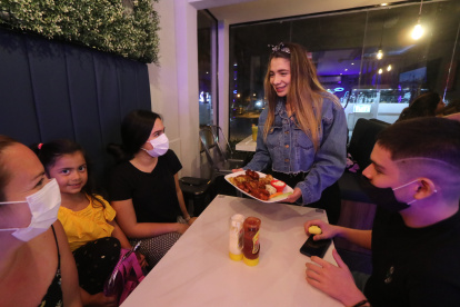 Katiuska González entrega el plato de alitas a una familia que llega a comer a su restaurante.