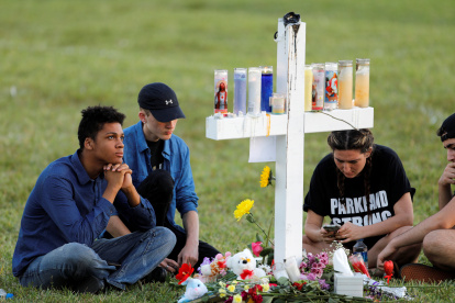 Mourners sit around one of 17 crosses at a memorial for the victims of the shooting at Marjory Stoneman Douglas High School in Parkland, Florida, U.S. February 16, 2018.  REUTERS/Jonathan Drake