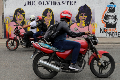 Dos motocicletas pasan frente a un mural que retrata a tres mujeres víctimas de violencia de género hoy, en Tegucigalpa (Honduras).
