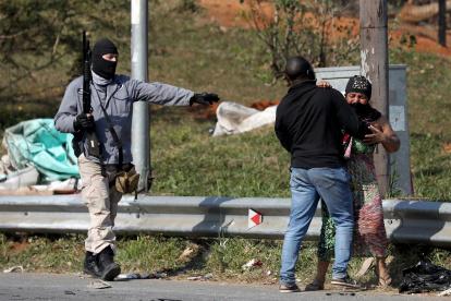 Un hombre calma a una mujer que recibió un disparo con una bala de goma mientras continúan los saqueos en Mobeni.