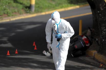 Un agente de la Dirección de Policía de Investigación inspecciona la escena donde un joven fue asesinado.