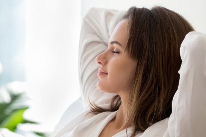 Beautiful 30s woman closed eyes put hands behind head relaxing on comfortable sofa in cozy warm light living room with houseplants, no stress concept, horizontal photo banner for website header design