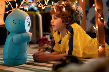 Un niño jugando con el robot Moxie en el suelo.