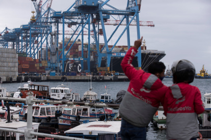 AME7422. VALPARAISO (CHILE), 12/11/2021.- Fotografía de archivo fechada el 15 de junio de 2020 que muestra a dos repartidores de domicilios mientras observan contenedores en el puerto de Valparaíso (Chile). Fertilizantes para la poderosa industria agropecuaria de Brasil, chips semiconductores para las automotrices mexicanas o falta de buques para exportar el café colombiano: Latinoamérica empieza también a sentir los efectos de la crisis global de suministros. Si bien la situación no es crítica, como en Estados Unidos, donde la campaña navideña está amenazada, la cadena de suministro en algunos países latinoamericanos comienza a estresarsel. EFE/ Alberto Valdés /ARCHIVO