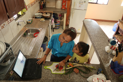 La profesora Carmita Agurto participa en una reunión de la escuela mientras atiende a una de sus hijas.