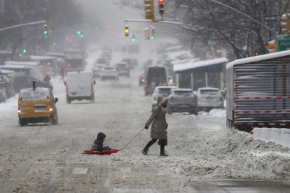 Una mujer y un niño sobre un trineo fueron registrados este sábado al cruzar una calle cubierta de nieve en Nueva York (NY, EE.UU.).