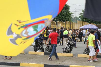 Una bandera de Ecuador y de fondo compradores de boletos para el partido entre Ecuador y Argentina en el Monumental