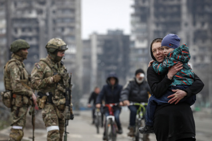 Mariúpol.  Varios civiles caminan, mientras militares ucranianos resguardan una avenida en esta ciudad puerto.