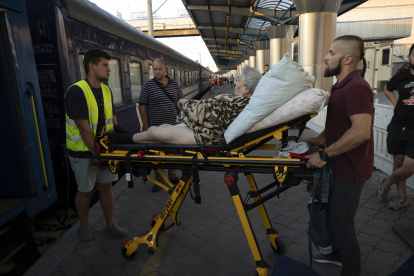 Voluntarios suben a una anciana a un vagón, donde van las personas que huyen de las zonas de combates en un tren de la "Ukrzaliznytsia", la empresa estatal de ferrocarriles, ayer en Dnipro (Ucrania). EFE/Orlando Barría