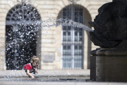 Un niño se rocía con agua de la fuente en la Place de la Bourse, durante la ola de calor, en la ciudad francesa de Burdeos.