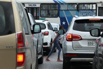Una  niña esquiva los autos del tráfico mientras intenta comercializar fundas de basura