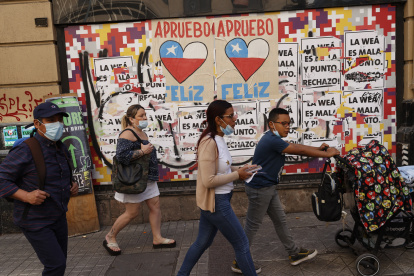 Varias personas caminan frente a una pared con información relacionada al plebiscito constitucional en Santiago (Chile).