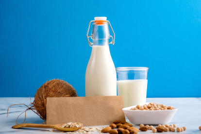 Lactose free milk. Bottle and glass of milk, almond nuts, oat flakes, coconut and piece of paper with text LACTOSE FREE on wooden surface on blue background. Lactose intolerance food concept