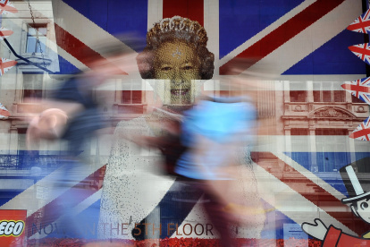 Unos niños corren frente a una imagen de la difunta reina Isabel II frente a la bandera de la Unión hecha completamente de lego en una tienda de juguetes en Londres.