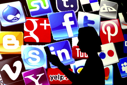 Una mujer revisa su teléfono frente a una pantalla que muestra los íconos de las redes sociales más populares.