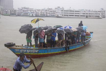 Los pasajeros de Bangladesh cruzan el río Buriganga mientras sostienen paraguas durante una fuerte lluvia y las duras condiciones causadas por el ciclón Sitrang EFE/EPA/MONIRUL ALAM