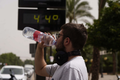 Un joven bebe agua junto a un termómetro de calle que marca 44º, en una fotografía de archivo.