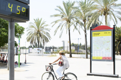 Sevilla. Una mujer en bicicleta pasa junto a un termómetro que marca 45 grados en una calle de esta urbe.