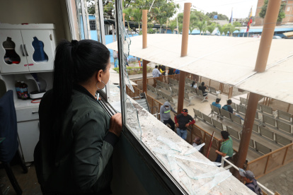 Destrucción. Entre los ventanales rotos de su departamento, Gabriela Pino observa los trabajos de reconstrucción en los bajos del edificio que fue afectado por la explosión de una bomba, afuera del Municipio de Durán.