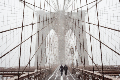 Fotografía de archivo en la que se registró a un par de transeúntes al cruzar el puente de Brooklyn, bajo una tormenta de viento y nieve, en Nueva York (NY, EE.UU.).