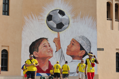 Un grupo de hinchas ecuatorianos reunidos en Qatar con una imagen alegórica al Mundial en un muro.