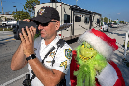 El  coronel de la oficina del alguacil del condado de Monroe, Lou Caputo, disfrazado de Grinch, y al diputado Andrew Leird mientras miden la velocidad de conductores en la autopista Florida Keys Overseas, en Marathon (Florida, EE.UU.). EFE/Andy Newman