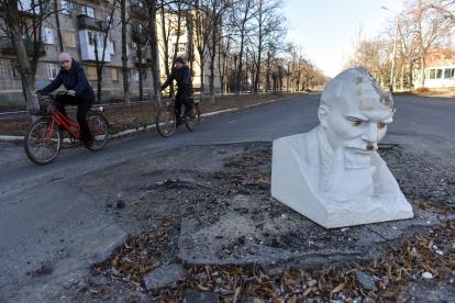 Dos personas en bicicleta pasan frente al busto de Vladimir Lenin, que cubre el cráter de los bombardeos en la carretera en la ciudad recuperada de Lyman, en la región de Donetsk, en el este de Ucrania.