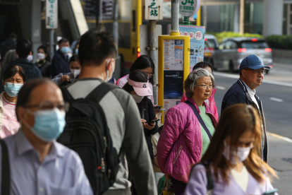 Viajeros, algunos de ellos todavía con mascarillas, esperan en una parada de autobús en Hong Kong, China, 01 de marzo de 2023