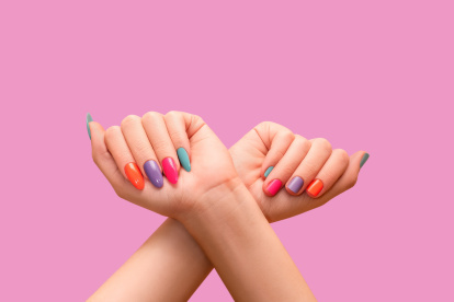 Female hands: one with long colorful nail design and other with short nail design. Glitter nail polish manicure: purple, green, pink, and orange. Female model hands with perfect colorful manicure on p