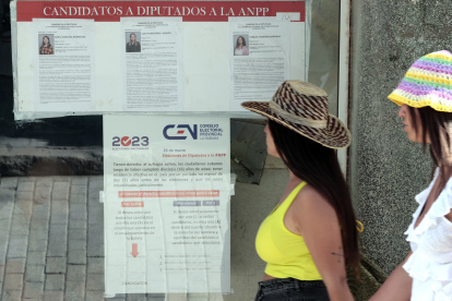 Dos mujeres pasan frente a unos carteles informativos sobre el proceso electoral del domingo.
