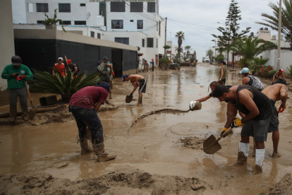 un grupo de personas al remover el lodo de una calle anegada por las lluvias, en el balneario de Punta Hermosa, al sur de Lima (Perú).