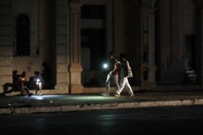 Personas caminan por una calle sin iluminación auxiliándose con la luz de su celular durante un apagón, en La Habana (Cuba).