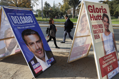 Personas caminan frente a carteles de propaganda electoral para consejeros Constitucionales, el 27 de abril 2023, en Santiago (Chile). Chile celebra este domingo sus segundas elecciones constituyentes en dos años, pero el contexto actual dista mucho de la efervescencia de 2021, cuando aún estaba presente el estallido de 2019, y la hoja de ruta acordada ahora para escribir la nueva Constitución es muy diferente. EFE/Elvis González