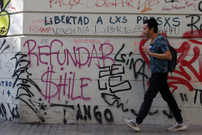 Un hombre camina frente a un mural pidiendo "Refundar Chile"