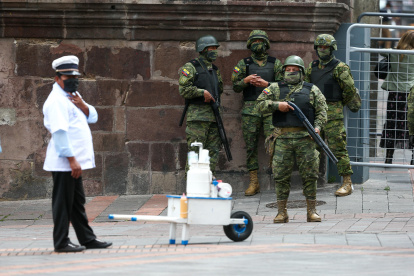 Militares y un vendedor  esperan a las afueras del Palacio de Gobierno en Quito.