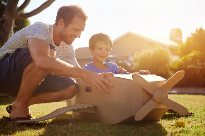 son and dad playing with toy aeroplane in the garden at home having fun together and smiling