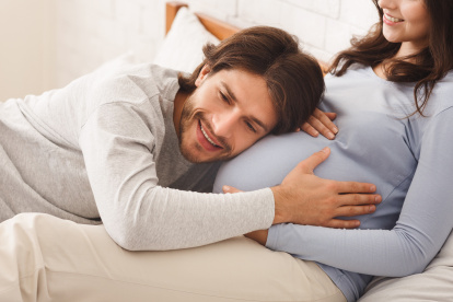 Pregnancy And Expectation concept. Future dad listening belly of his pregnant wife while lying on bed together, panorama