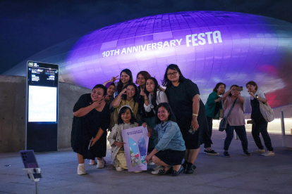 Turistas extranjeros se toman una foto frente a Dongdaemun Design Plaza en Seúl, Corea del Sur, iluminado de púrpura la noche del 12 de junio de 2023, como parte de un festival de dos semanas para celebrar el décimo aniversario de la sensación mundial del K-pop BTS debut, que cae el 13 de junio.