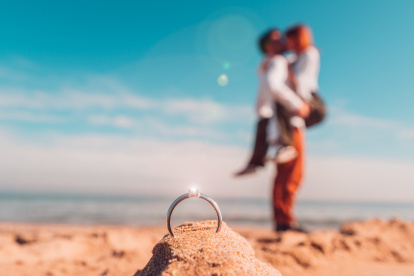 Romantic marriage proposal on the beach at the seaside. Couple in love kissing outdoor with a marriage ring in front of them.
