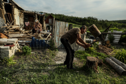 Mykola (R), de 58 años, corta leña mientras su madre Nina, de 92, se sienta en su patio entre los restos de su casa en el pueblo de Bohorodychne, región de Donetsk, Ucrania