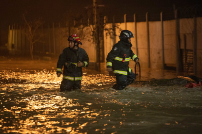 Bomberos caminan en la madrugada de hoy por calles anegadas por agua tras la crecida del río Cachapoal, producto de las intensas lluvias en la comuna de Coltauco (Chile). Miles de chilenos permanecen aislados o damnificados a causa de las lluvias torrenciales que se presentan desde el jueves pasado en el centro del país, una situación anormal producto de las altas temperaturas en las cimas de Los Andes, inusuales en este inicio del invierno austral, y que ya deja dos muertos y seis desaparecidos, dijeron este domingo las autoridades. EFE / Rafael Arancibia