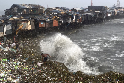 Un hombre se ve sorprendido por una ola mientras rescata materiales desperdigados por la orilla en Manila Bay, Filipinas, este miércoles.