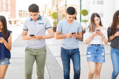 Group of five young boys ands girls walking outdoors in city with their smart phones