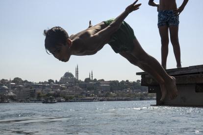 En la imagen de archivo, una persona se sumerge en las aguas del Bósforo para refrescarse, con la mezquita de Süleymaniye al fondo, en Estambul, Turquía.