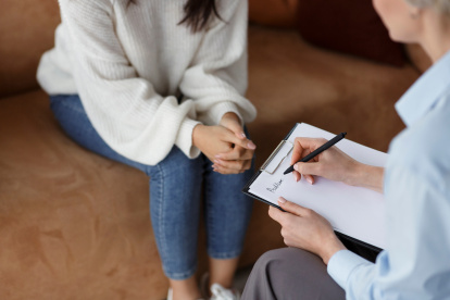 Unrecognizable Psychologist Talking With Female Client Taking Notes During Psychotherapy Session Sitting In Office. Selective Focus, Cropped